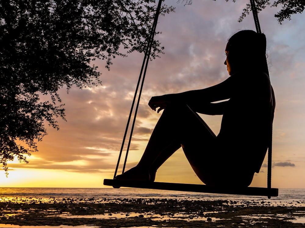 silhouette of person sitting on swing, watching sunset