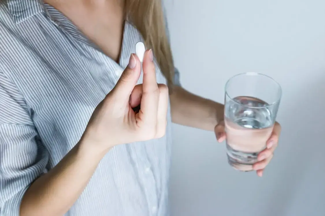 woman holding white pill and glass of water