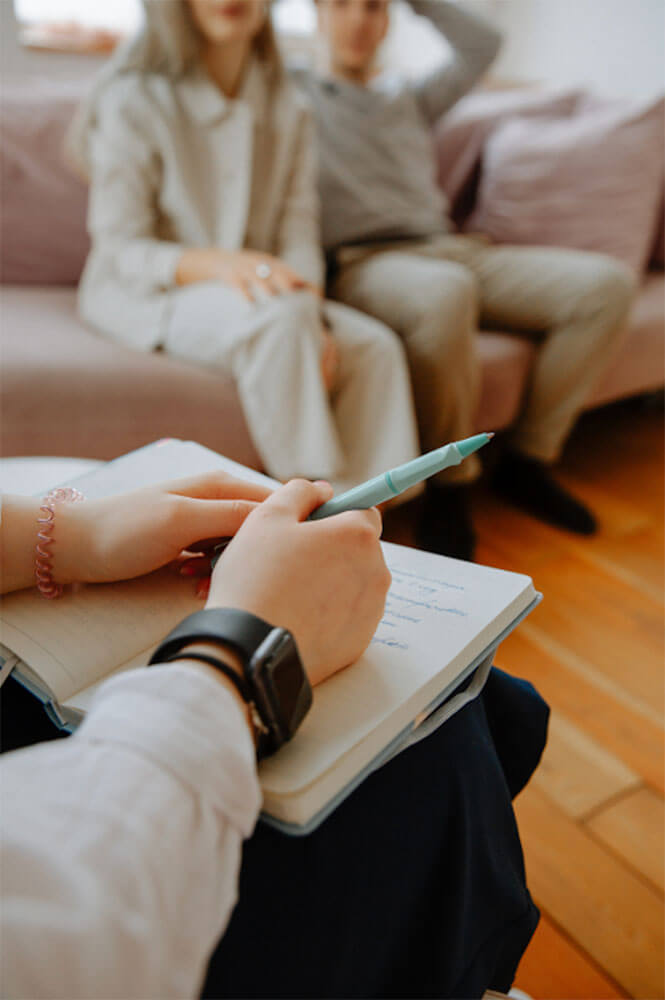 Couples-1 couple seated together on couch, each holding ring fingers