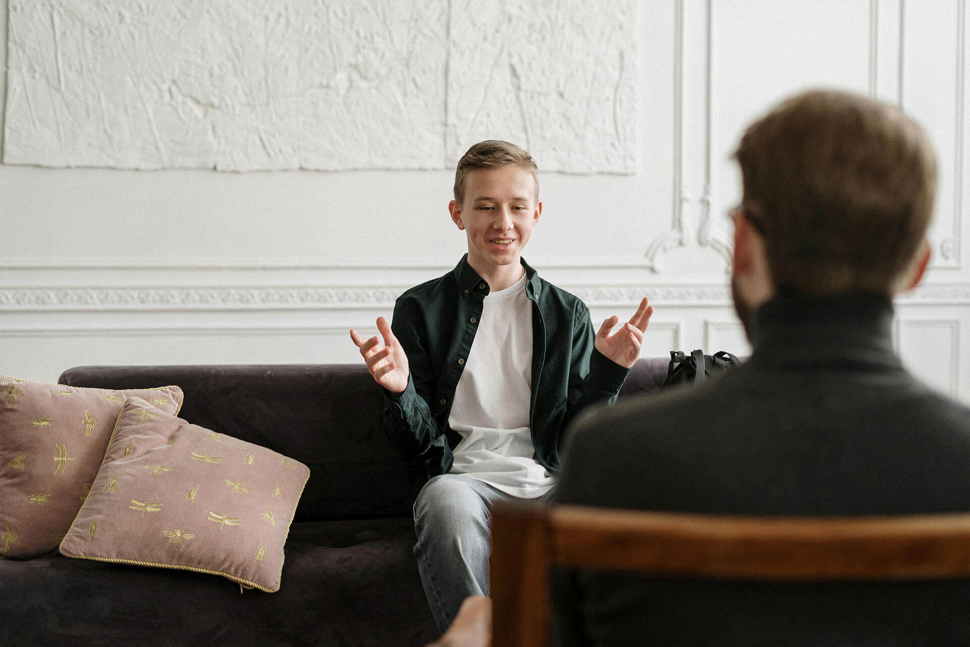 A young man sitting on a couch, and talking to a person sitting across from him