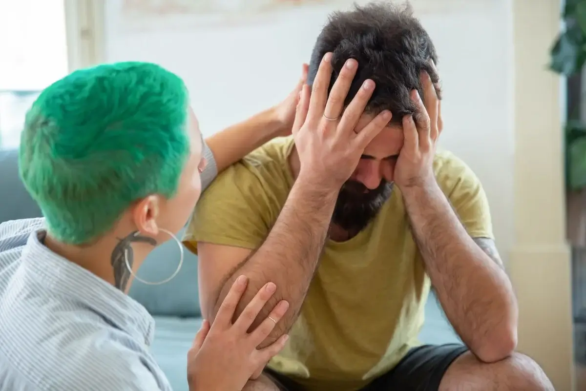 A man with his head in his hands as a woman with green hair comforts him